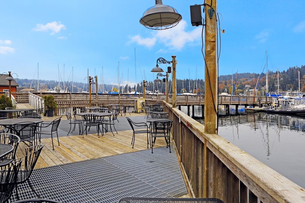 Large deck on water with dining table sets. View of dock and boats. Gig Harbor.